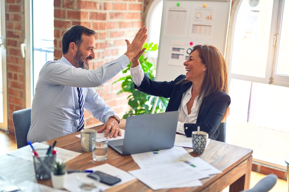 Two consultants celebrating a win with a client at a desk
